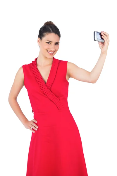 Happy elegant brunette in red dress taking picture — Stock Photo, Image