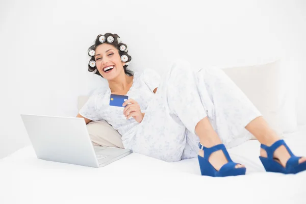 Morena em rolos de cabelo e sapatos cunha usando seu laptop para fazer compras on-line — Fotografia de Stock