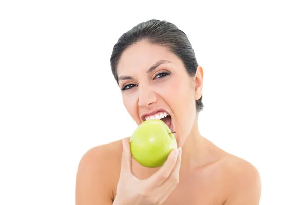 Glückliche Brünette isst einen grünen Apfel und schaut in die Kamera — Stockfoto