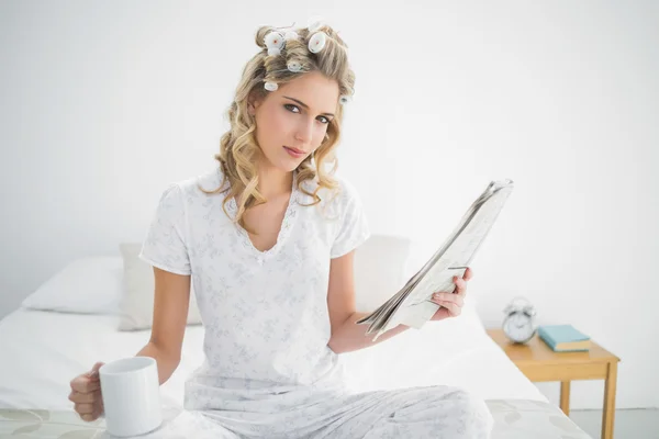 Peaceful cute blonde wearing hair curlers holding newspaper — Stock Photo, Image