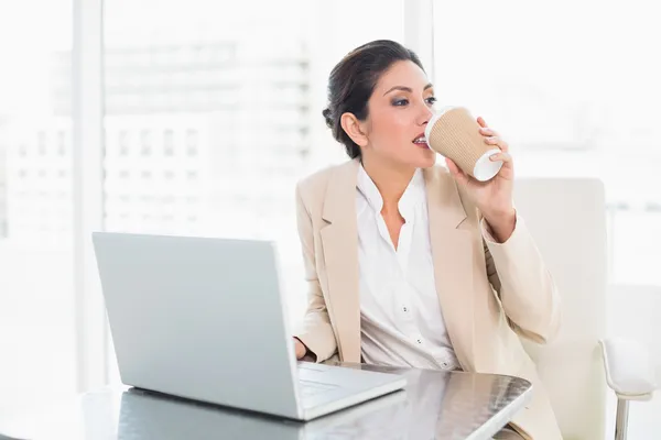 Стильная деловая женщина пьет кофе во время работы на ноутбуке — стоковое фото
