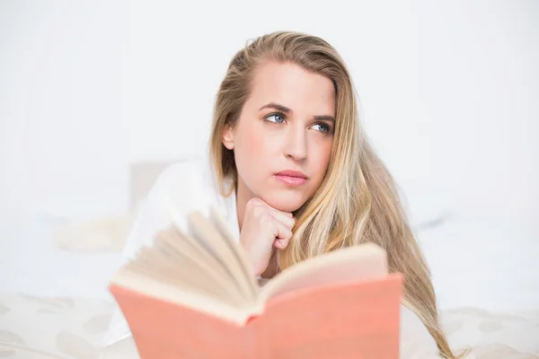 Pensativo hermosa modelo acostado en la cama acogedora celebración de libro —  Fotos de Stock