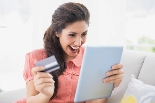 Ecstatic brunette sitting on her sofa using tablet to shop online — Stock Photo, Image