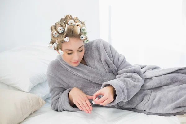 Koncentrovaná uvolněná blondýnka v použití lak natáčky na vlasy — Stock fotografie