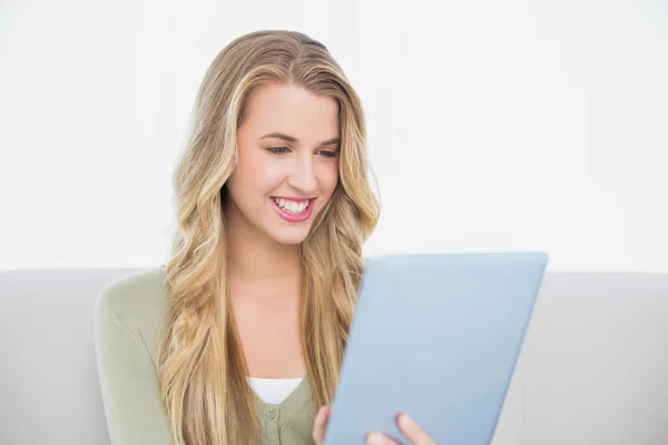 Smiling pretty blonde using her tablet sitting on cosy sofa — Stock Photo, Image