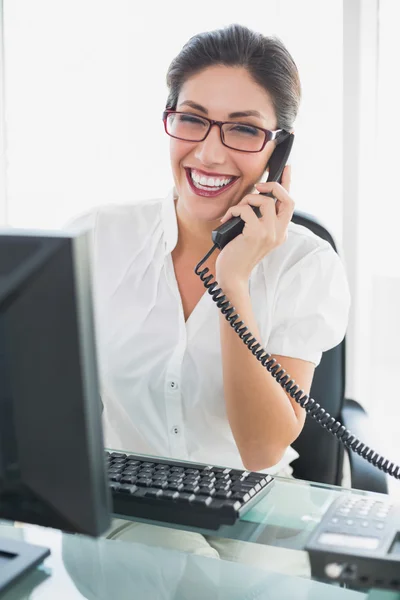 Uśmiechnięta kobieta siedzi przy biurku, rozmawia przez telefon — Zdjęcie stockowe