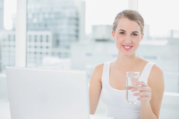 Roztomilá blondýnka drží sklenici vody pomocí její laptop — Stock fotografie