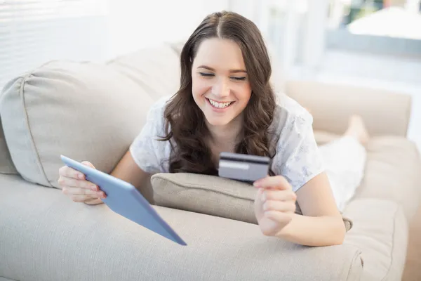 Cheerful woman lying on a cosy couch buying online — Stock Photo, Image