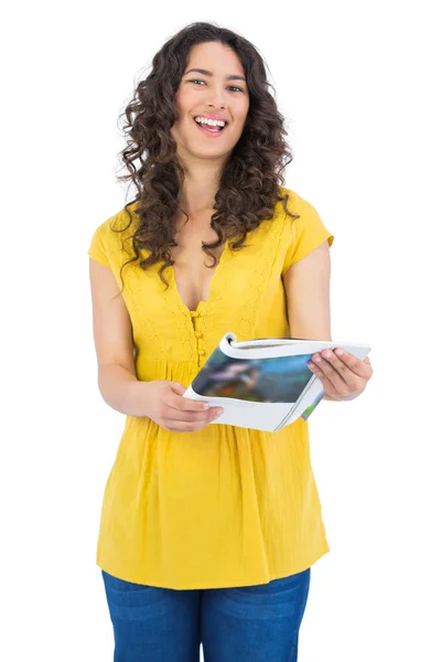Curly haired brunette laughing while reading magazine — Stock Photo, Image