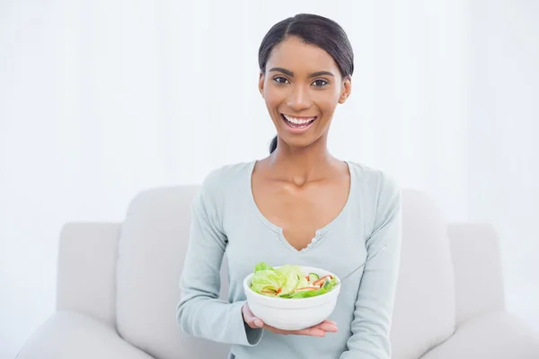 Lachende aantrekkelijke vrouw die zit op de gezellige sofa houden salade — Stockfoto