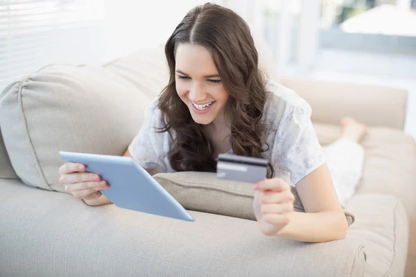 Усміхнена жінка лежить на затишному дивані, купуючи онлайн — стокове фото