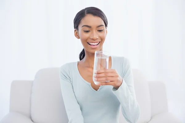 飲料水の居心地の良いソファの上に座って魅力的な女性は笑みを浮かべて — ストック写真
