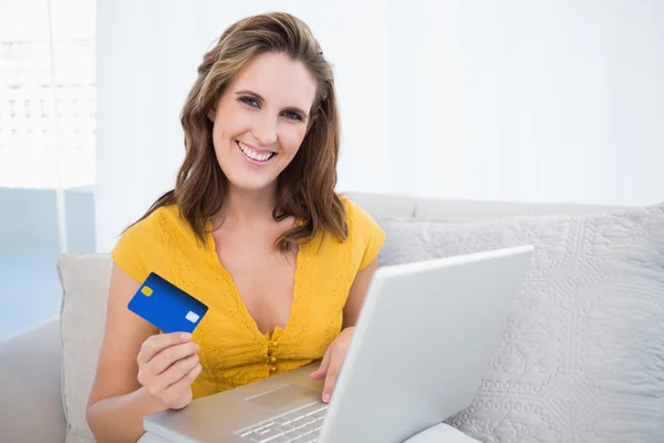 Усміхнена жінка тримає ноутбук, що показує кредитну картку — стокове фото