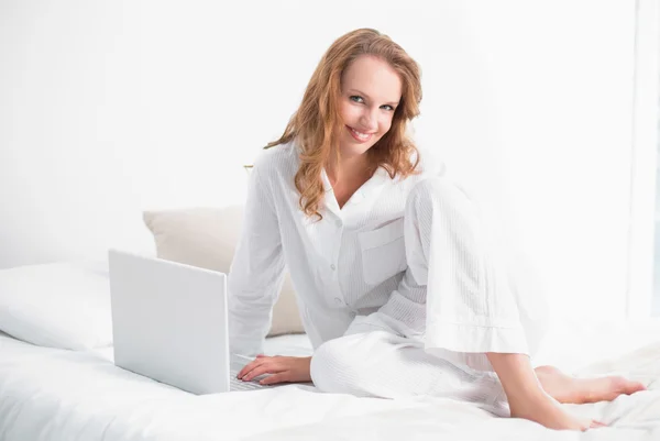 Zufriedene hübsche Frau mit Laptop auf ihrem Bett sitzend — Stockfoto