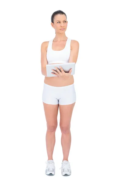Вдумчивая женщина в спортивной одежде с помощью планшетного компьютера — стоковое фото