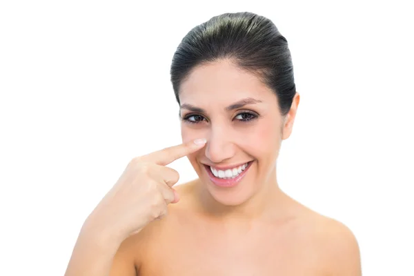 Smiling brunette pointing to nose and looking at camera — Stock Photo, Image