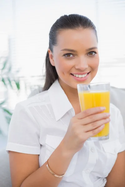 Cheerful pretty woman holding orange juice sitting on cosy couch — Stock Photo, Image