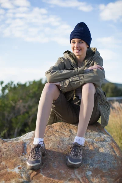 Mujer sonriente con gorra sentada en una roca — Foto de Stock