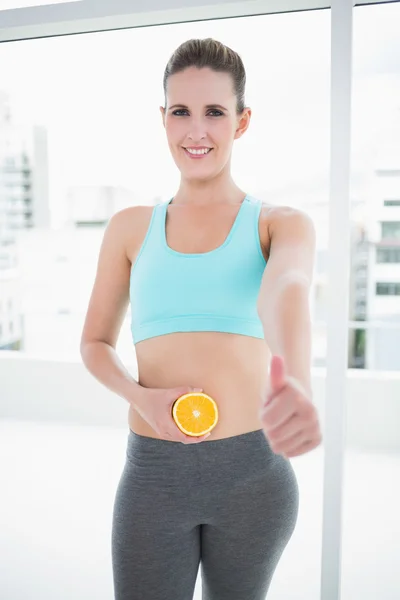 Smiling woman in sportswear holding orange slice on her belly — Stock Photo, Image
