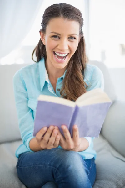 Sorrindo mulher sentada no sofá segurando livro — Fotografia de Stock