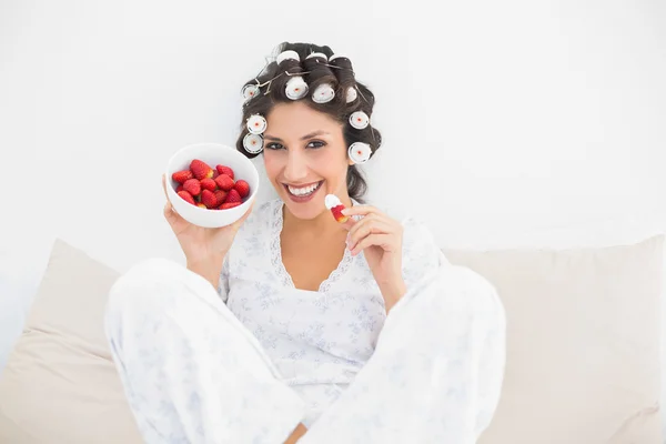 Joyeux brunette en rouleaux de cheveux ayant un bol de fraises — Photo