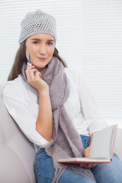 Thoughtful pretty brunette with winter hat on holding notebook — Stock Photo, Image