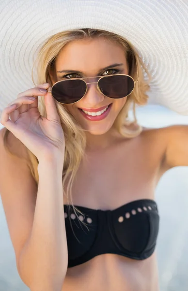 Rubia sonriente en elegante bikini negro mirando por encima de sus gafas de sol — Foto de Stock