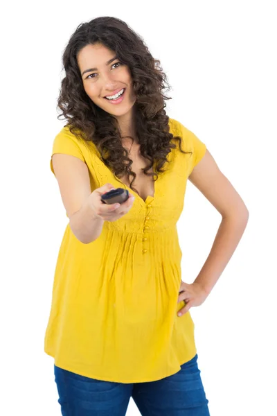 Smiling curly haired pretty woman changing channel with remote — Stock Photo, Image