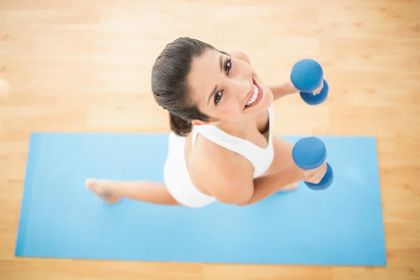 Mujer feliz haciendo ejercicio con mancuernas en alfombra de ejercicio azul — Foto de Stock
