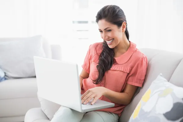 Gelukkig brunette zittend op haar bank met behulp van laptop — Stockfoto