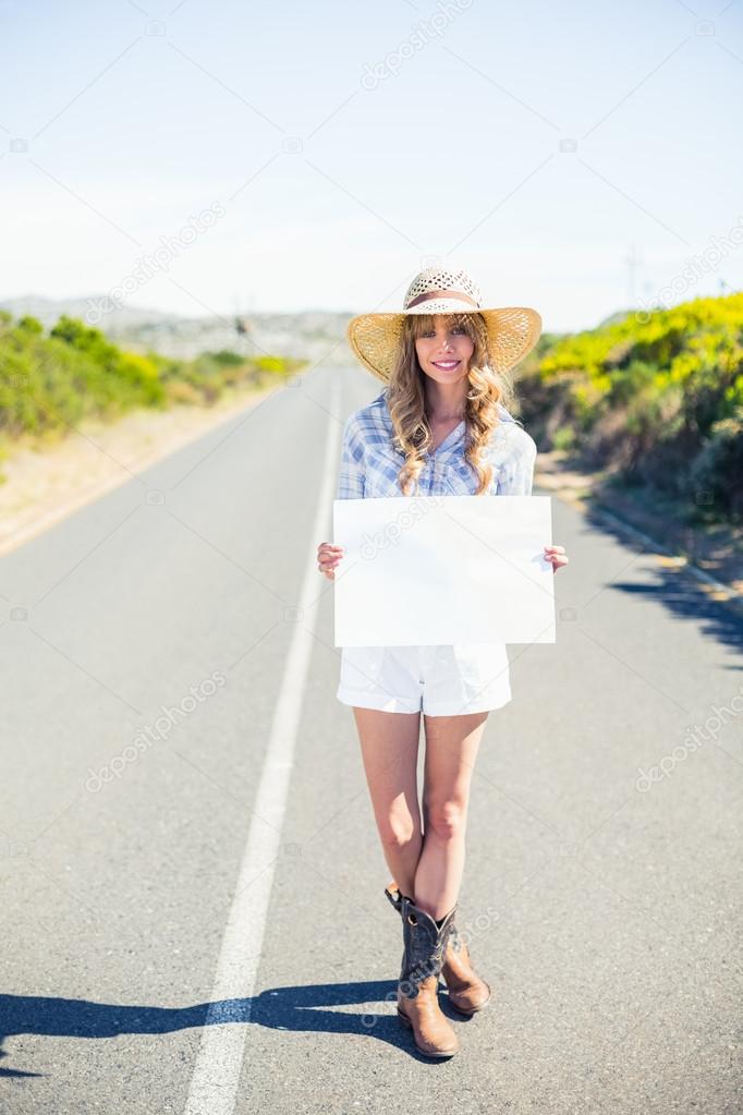 Smiling blonde holding sign while hitchhiking on the road