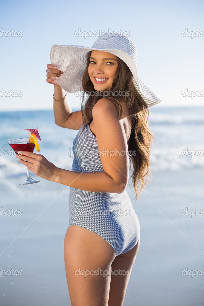 Gorgeous woman in swimsuit holding cocktail looking over shoulde