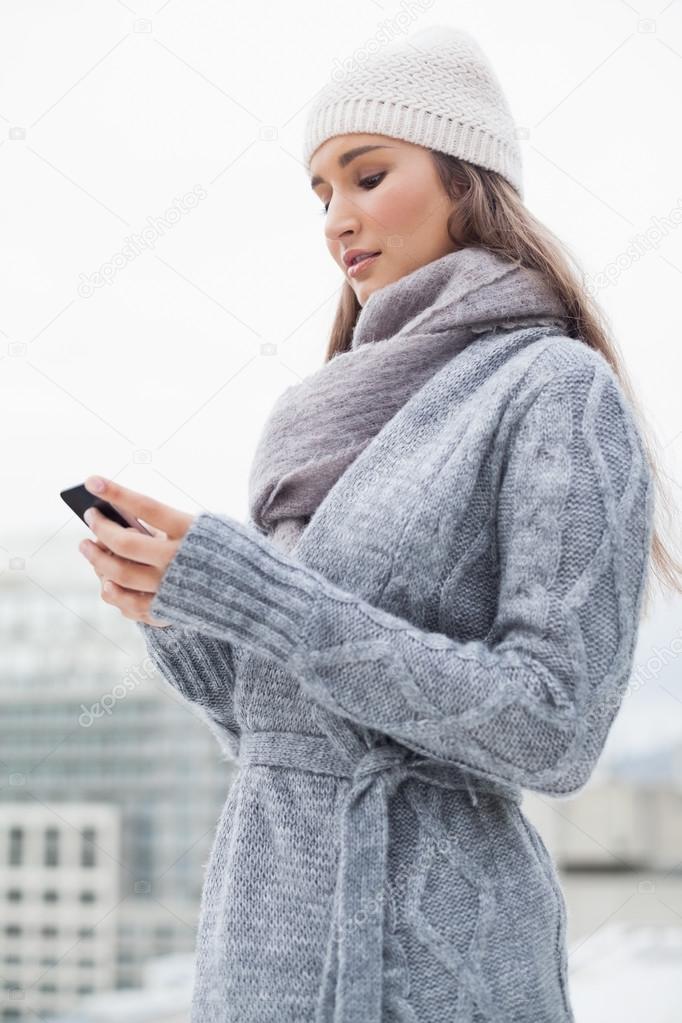 Focused brunette with winter clothes on text messaging