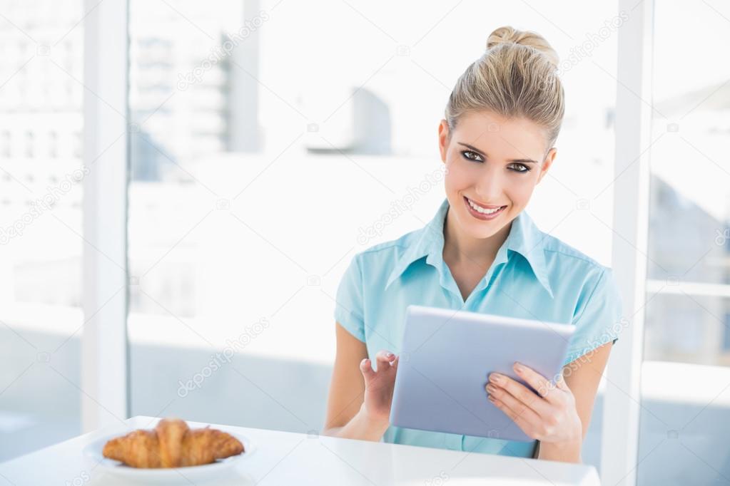 Smiling classy woman using tablet while having breakfast