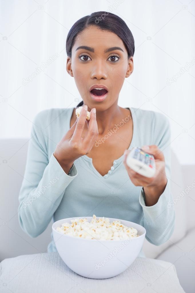 Astonished attractive woman eating popcorn while watching tv