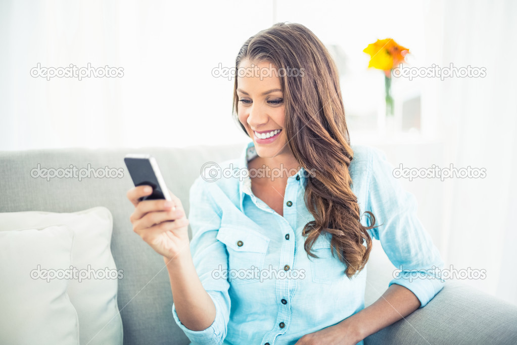 Smiling model sitting on cosy couch texting