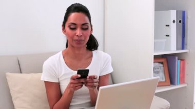 çekici bir kadın kanepe manifatura telefon üzerinde dizlerinin üstünde laptop ile oturup...