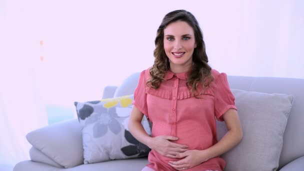 Pretty pregnant model sitting on her couch smiling at camera — Stock Video