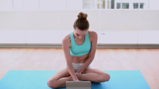 Подходящая модель, сидящая на коврике для упражнений с помощью планшетного компьютера — стоковое видео
