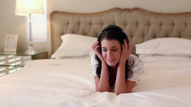 Красивая брюнетка лежит на кровати и слушает музыку. — стоковое видео