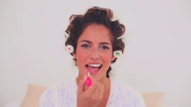 Pleased woman in hair curlers applying gloss — Stock Video