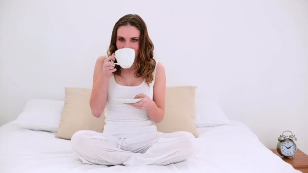 Hübsches Modell sitzt auf dem Bett und trinkt eine Tasse Kaffee — Stockvideo