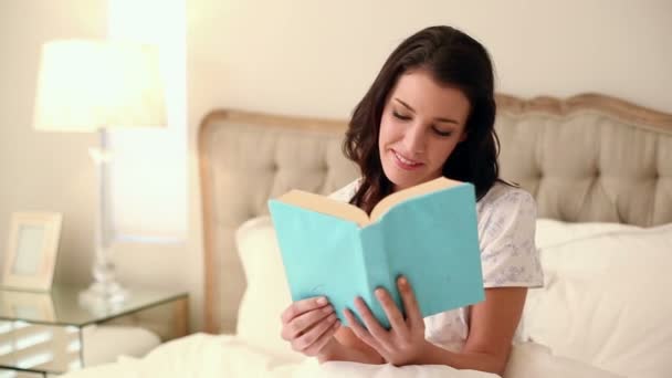 Hermosa morena sentada en la cama leyendo un libro — Vídeos de Stock
