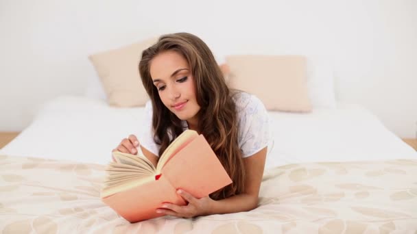Молодая женщина читает книгу, лежащую на кровати — стоковое видео