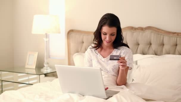 Schöne Brünette mit ihrem Laptop im Bett sitzen, um online einzukaufen — Stockvideo