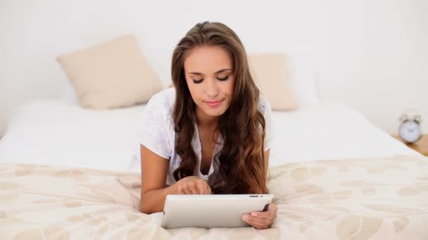 Mujer joven usando su tableta acostada en su cama — Vídeo de stock