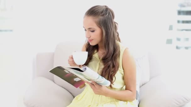 Mujer joven bebiendo café y leyendo una revista en el sofá — Vídeos de Stock