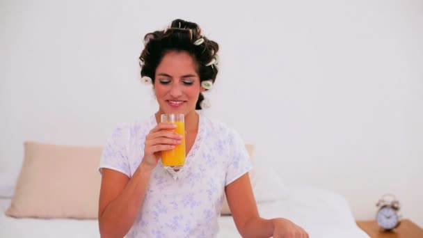 Mulher alegre em encrespadores de cabelo desfrutando de suco de laranja — Vídeo de Stock