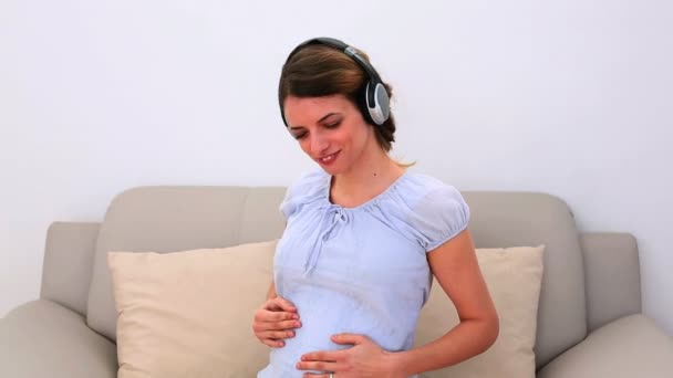 Mujer embarazada escuchando música en el sofá — Vídeo de stock