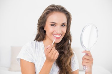 Brunette applying lip gloss and holding mirror